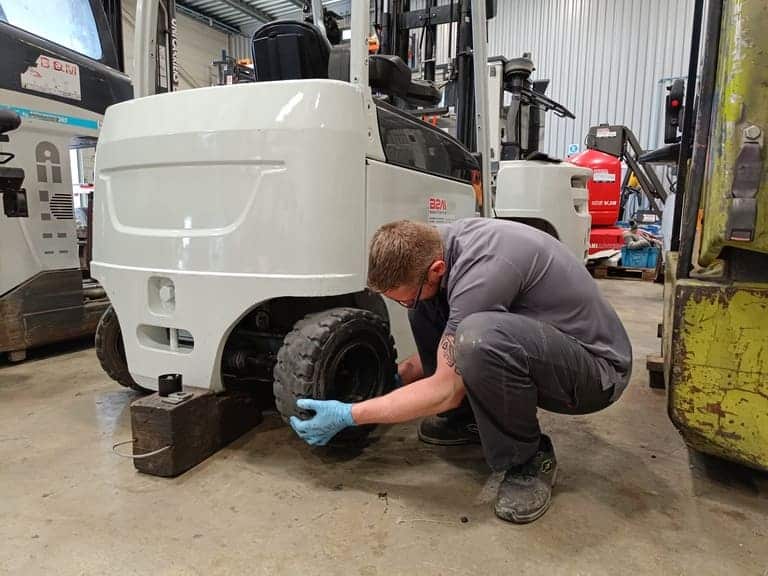 Image d'un technicien de maintenance B2M Manutention qui réalise le remplacement d'un pneu de chariot élévateur